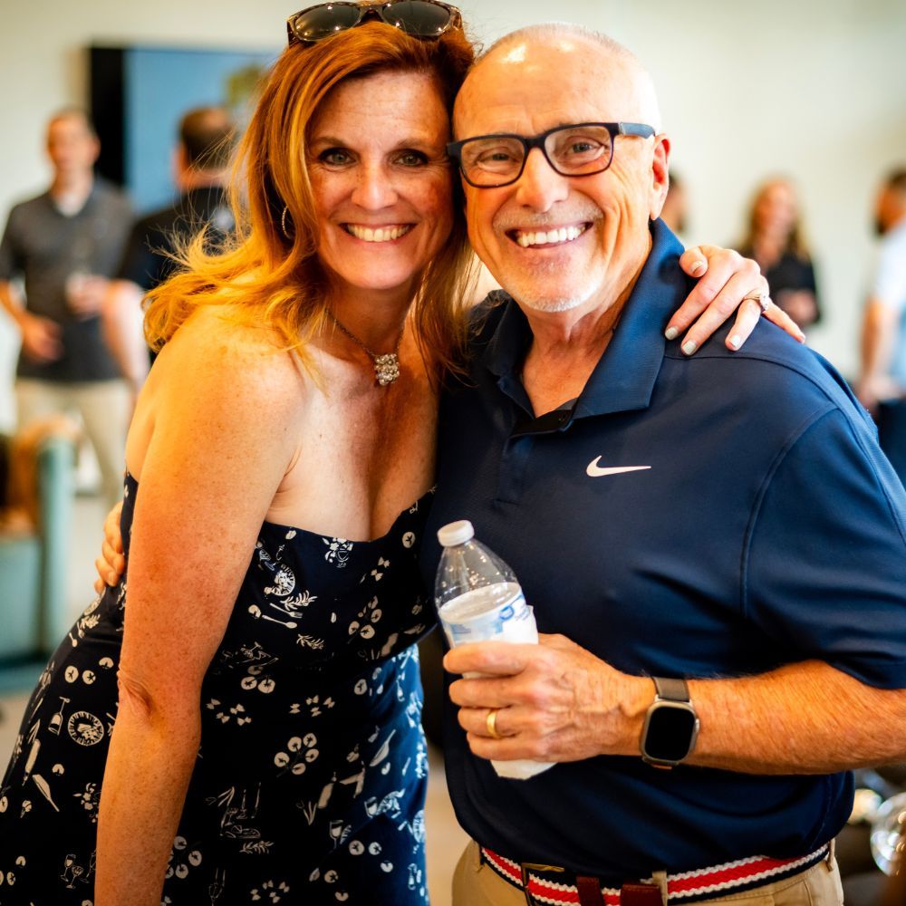 Smiling woman and man pose together at an indoor event; man holds a water bottle.